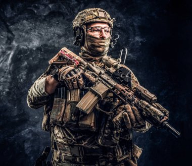 Asker kamuflaj bir saldırı tüfeği tutan tek tip içinde tam donanımlı. Karanlık bir duvara Studio fotoğraf