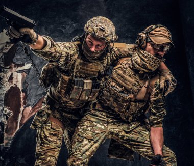 Combat conflict, special mission. The military soldier carrying teammate out of the battlefield. Studio photo against a dark wall