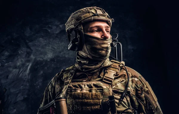 Moderno soldato delle forze speciali in uniforme mimetica guardando lateralmente. Studio foto contro un muro scuro . — Foto Stock