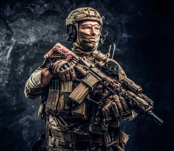 Soldado totalmente equipado em uniforme de camuflagem com uma espingarda de assalto. Foto de estúdio contra uma parede escura — Fotografia de Stock