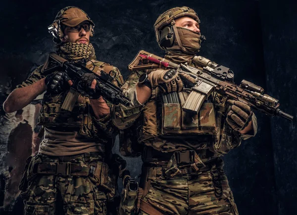 Deux soldats des forces spéciales en équipement de protection complet avec fusils d'assaut. Studio photo contre un mur sombre . — Photo