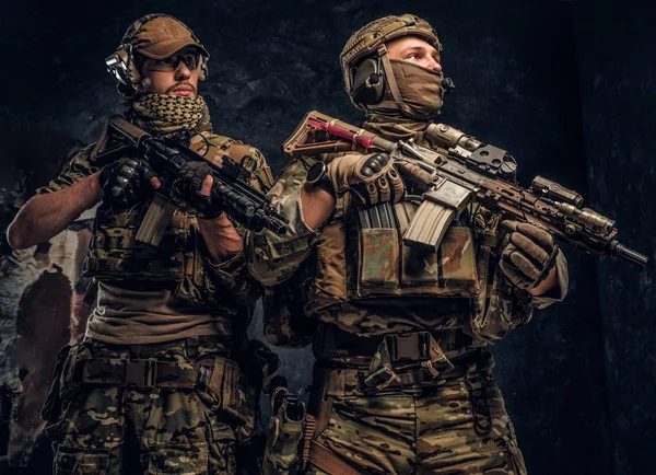 Dos soldados de las fuerzas especiales en equipo de protección completa con rifles de asalto. Foto del estudio contra una pared oscura . — Foto de Stock