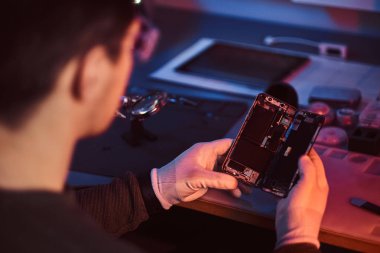 Tamirci dikkatle smartphone içinde modern bir tamirciye iç unsurları bütünlüğünü inceler. Kırmızı ve Mavi ışıklı aydınlatma
