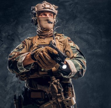 Bir el feneri ile silah doğrultmak ve yana doğru seyir kamuflaj üniformalı Özel Kuvvetler asker. Studio fotoğraf bir karanlık dokulu duvara