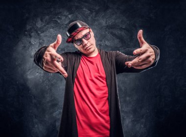 Hip-hop tarzında, bir kamera için poz giyinmiş genç rapçi portresi. Karanlık bir duvara Studio fotoğraf