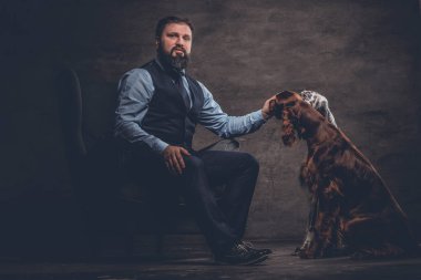 Onun iki safkan Setter köpek ile bir kanepede oturan zarif kıyafetlerle sakallı avcı.