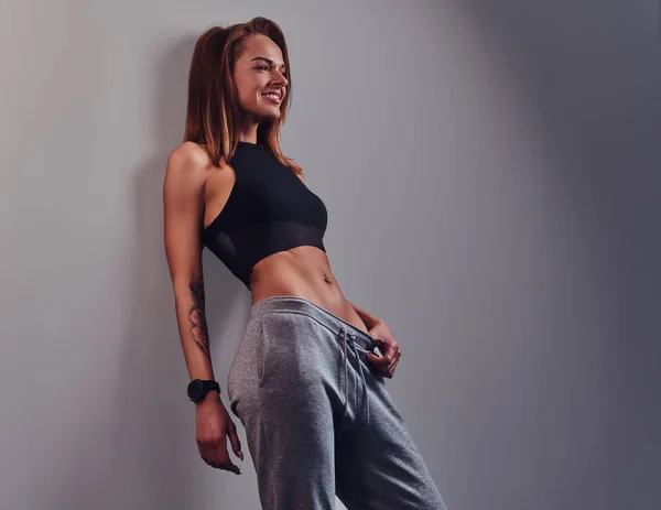 Mode, sport, santé. Mince fille de fitness portant des vêtements de sport appuyé sur un mur dans un studio . — Photo