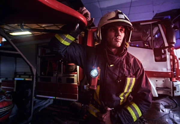 Portrait of a handsome fireman wearing a protective uniform with flashlight included standing in a fire station garage — Stock Photo, Image