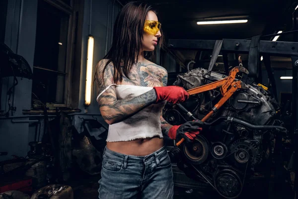 Female car mechanic working with an engine suspended on a hydraulic hoist in the workshop. — Stock Photo, Image