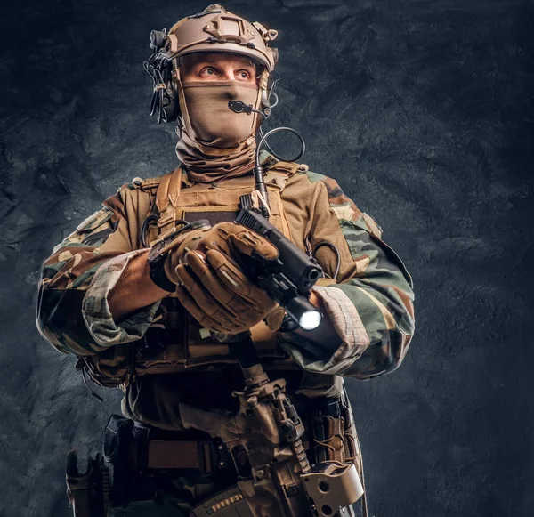 Bir el feneri ile silah doğrultmak ve yana doğru seyir kamuflaj üniformalı Özel Kuvvetler asker. Studio fotoğraf bir karanlık dokulu duvara