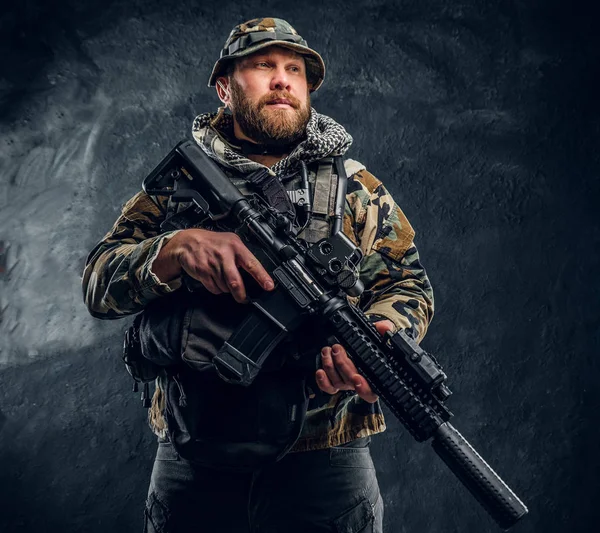 Soldado das forças especiais no uniforme camuflado militar segurando um rifle de assalto. Foto do estúdio contra uma parede de textura escura — Fotografia de Stock