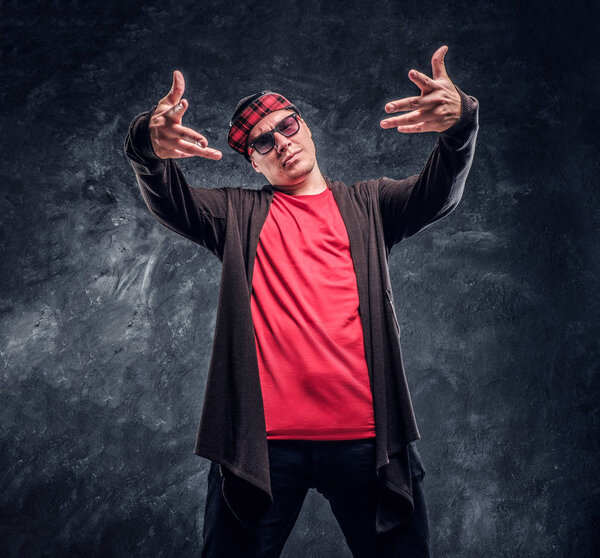Portrait of a young rapper dressed in a hip-hop style, posing for a camera. Studio photo against a dark wall