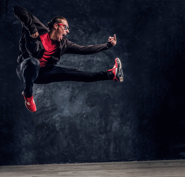 Emotional hip-hop style dancer performing acrobatic elements, jumping and shows the fuck sign.