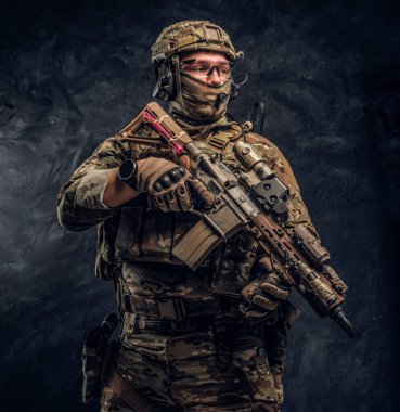 Asker kamuflaj bir saldırı tüfeği tutan tek tip içinde tam donanımlı. Karanlık bir duvara Studio fotoğraf