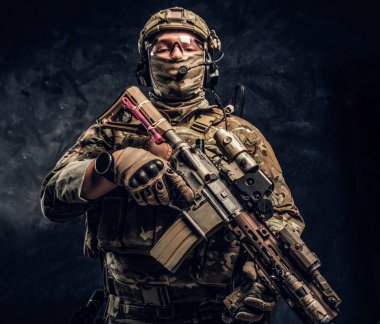 Asker kamuflaj bir saldırı tüfeği tutan tek tip içinde tam donanımlı. Karanlık bir duvara Studio fotoğraf
