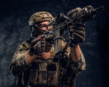 Elit birimi, Özel Kuvvetler asker bir saldırı tüfeği bir lazer görme ve amaçlar ile hedef kamuflaj üniformalı. Karanlık bir duvara Studio fotoğraf  