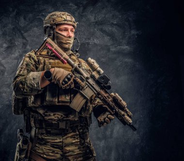 Asker kamuflaj bir saldırı tüfeği tutan tek tip içinde tam donanımlı. Karanlık bir duvara Studio fotoğraf