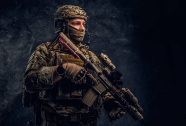 Asker kamuflaj bir saldırı tüfeği tutan tek tip içinde tam donanımlı. Karanlık bir duvara Studio fotoğraf