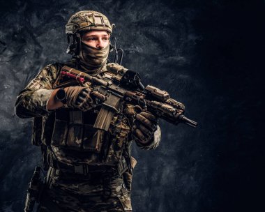 Asker kamuflaj bir saldırı tüfeği tutan tek tip içinde tam donanımlı. Karanlık bir duvara Studio fotoğraf