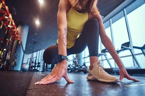 Mulher fitness bonita vestindo sportswear em pé na posição inicial, pronto para correr, no ginásio moderno . — Fotografia de Stock