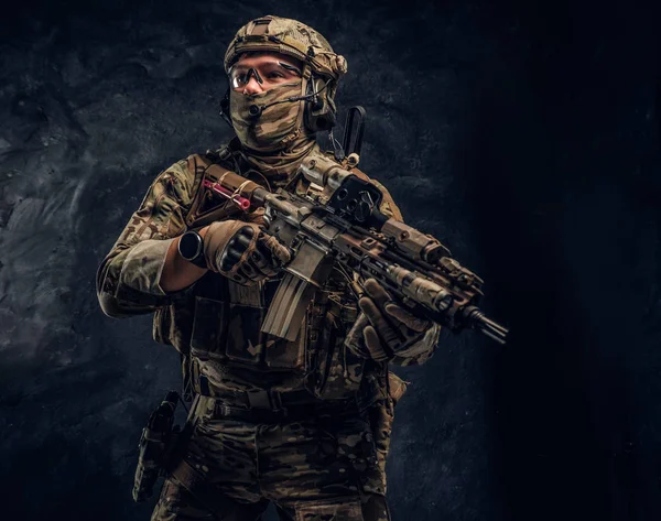 Soldado totalmente equipado em uniforme de camuflagem com uma espingarda de assalto. Foto de estúdio contra uma parede escura — Fotografia de Stock