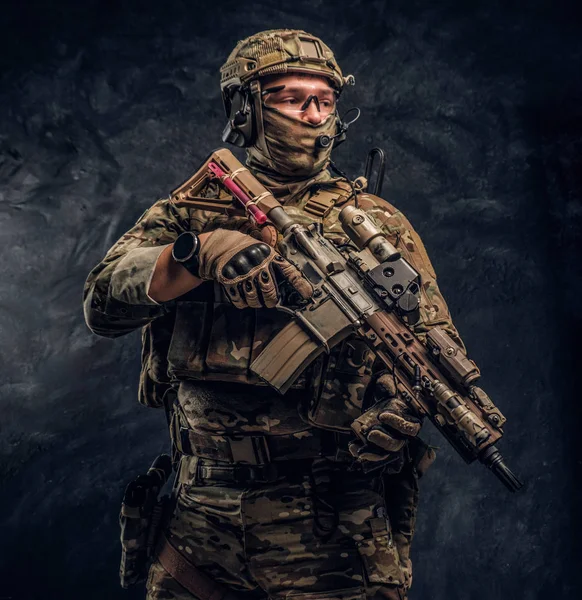 Soldado totalmente equipado con uniforme de camuflaje que sostiene un rifle de asalto. Foto del estudio contra una pared oscura —  Fotos de Stock