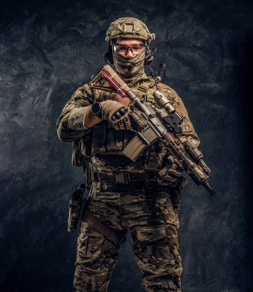 Soldado totalmente equipado con uniforme de camuflaje que sostiene un rifle de asalto. Foto del estudio contra una pared oscura — Foto de Stock