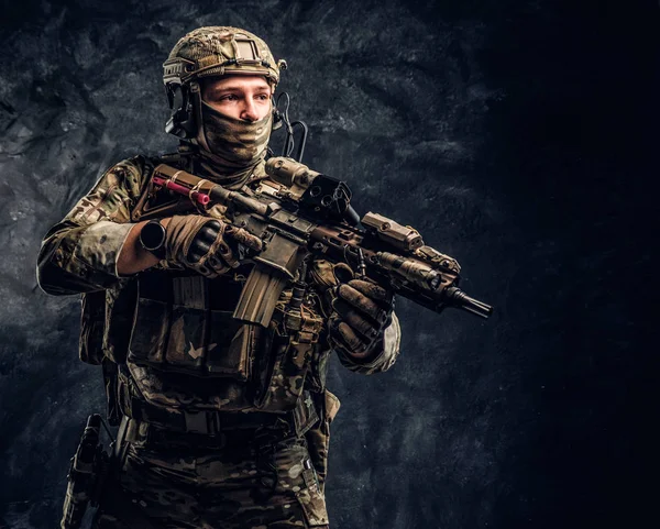 Soldado totalmente equipado con uniforme de camuflaje que sostiene un rifle de asalto. Foto del estudio contra una pared oscura —  Fotos de Stock