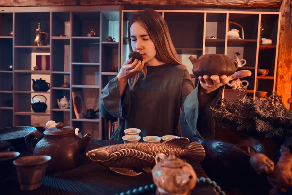Cérémonie du thé chinois. Maître oriental portant une robe grise tenant une théière et respire l'arôme du thé naturel frais dans la pièce sombre avec un intérieur en bois . — Photo