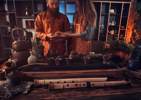 Cérémonie du thé chinois. Couple en vêtements traditionnels orientaux boit du thé naturel lors d'une cérémonie du thé chinois dans la pièce sombre avec un intérieur en bois . — Photo