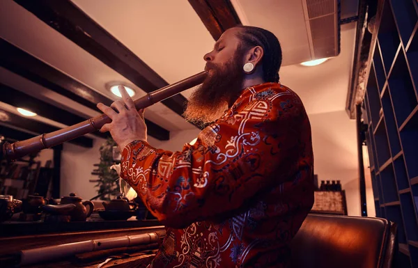 Traditie, gezondheid, harmonie. Chinese thee ceremonie. Thee meester in kimono presteert in de donkere kamer met een houten interieur, spelen op een bamboefluit — Stockfoto