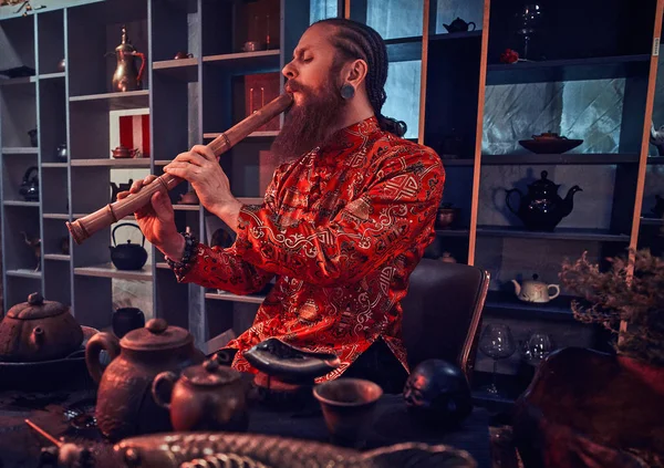 Tradição, saúde, harmonia. Cerimônia de chá chinês. Mestre de chá em quimono executa no quarto escuro com um interior de madeira, jogando em uma flauta de bambu — Fotografia de Stock