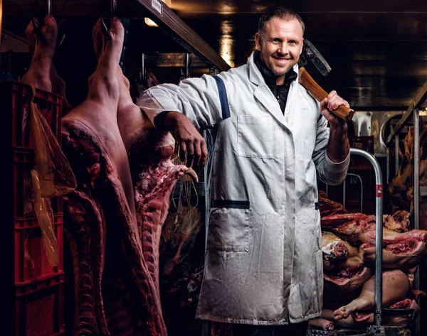 Açougueiro com uma camisa branca segurando machado enquanto estava em um armazém refrigerado no meio de carcaças de carne — Fotografia de Stock