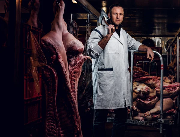 Açougueiro com uma camisa branca segurando machado enquanto estava em um armazém refrigerado no meio de carcaças de carne — Fotografia de Stock