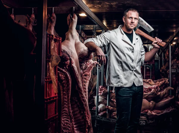 Açougueiro com uma camisa branca segurando machado enquanto estava em um armazém refrigerado no meio de carcaças de carne — Fotografia de Stock