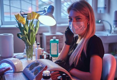 Maske ve eldiven ana güzellik uzmanı manikür masada oturur ve kameraya benziyor.