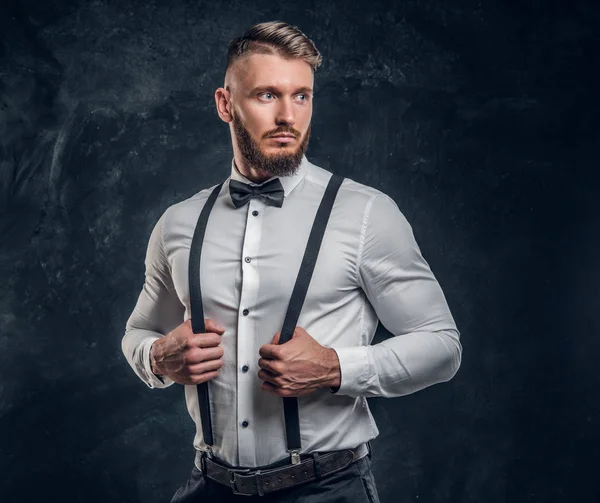 Jeune homme élégamment habillé en chemise avec nœud papillon et bretelles. Studio photo sur fond de mur sombre — Photo