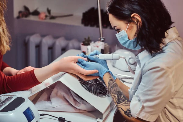 Kosmetikerin mit Handschuhen, die Nagelbohrer anwenden, um Nagelhaut zu schneiden und zu entfernen. Hardware-Maniküre im Schönheitssalon — Stockfoto