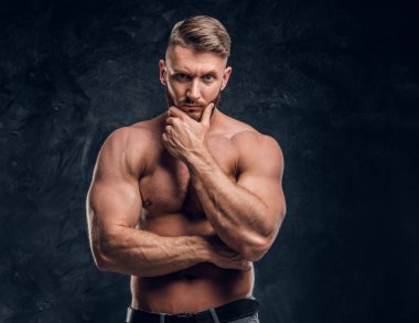 Gömleksiz erkek kas vücut çene üzerinde el ile poz ile sakallı. Studio fotoğraf bir karanlık duvar arka plan