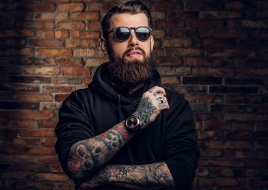 Bir siyah hoodie ve güneş gözlüğü bir şık dövmeli adam. Studio fotoğraf duvara karşı