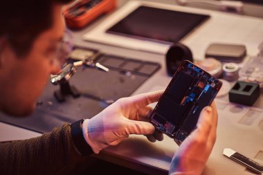 Teknisyen dikkatle smartphone içinde modern bir tamirciye iç unsurları bütünlüğünü inceler