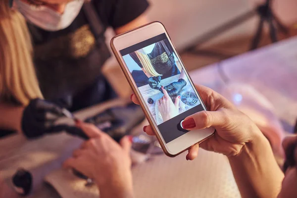 Woman takes a photograph of the manicure procedure in the beauty salon