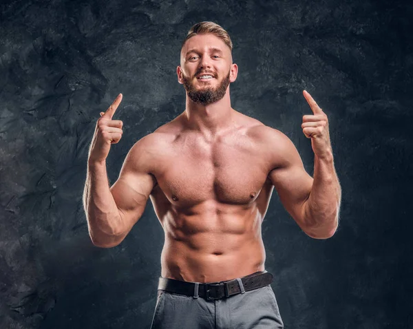 Um homem sem camisa alegre com o corpo muscular posando para uma câmera. Foto do estúdio contra fundo de parede escura — Fotografia de Stock