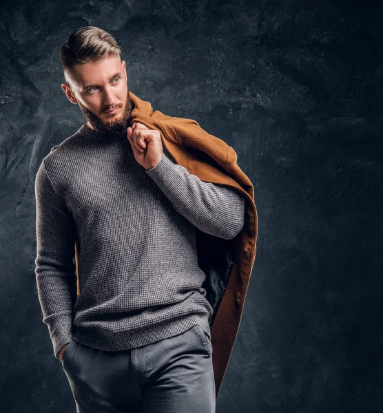 Pánské krása, sezónní módy. Portrét stylový muž drží jeho celosezónní plášť. Studiové fotografie pozadí tmavé stěny — Stock fotografie