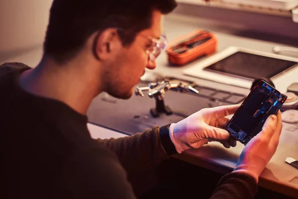 Tekniker undersöker noggrant integriteten i de inre delarna av smartphonen i en modern verkstad — Stockfoto