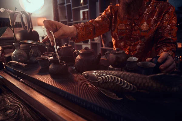 Кавказский мастер в кимоно делает натуральный чай в темной комнате с деревянным интерьером. Традиции, здоровье, гармония. Китайский чай — стоковое фото
