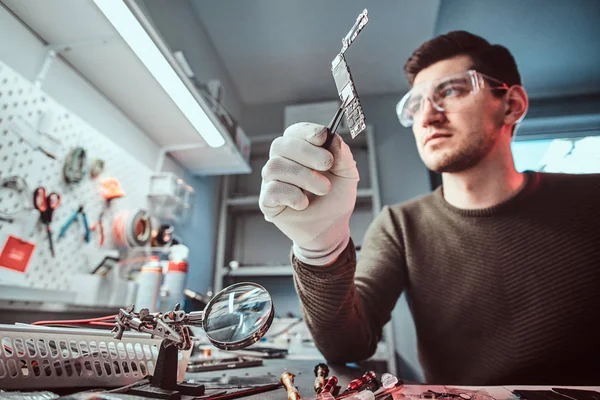 Meister der Elektrotechnik hält Chip eines kaputten Tablets in der Werkstatt — Stockfoto