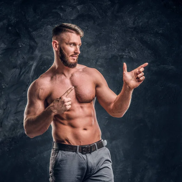 Um homem sem camisa alegre com o corpo muscular posando para uma câmera. Foto do estúdio contra fundo de parede escura — Fotografia de Stock