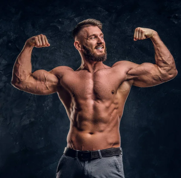 Modelo masculino con el cuerpo muscular posando para una cámara. Foto del estudio contra un fondo de pared oscuro — Foto de Stock