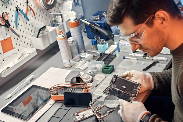 Técnico examina cuidadosamente la integridad de los elementos internos del teléfono inteligente en un taller de reparación moderno —  Fotos de Stock